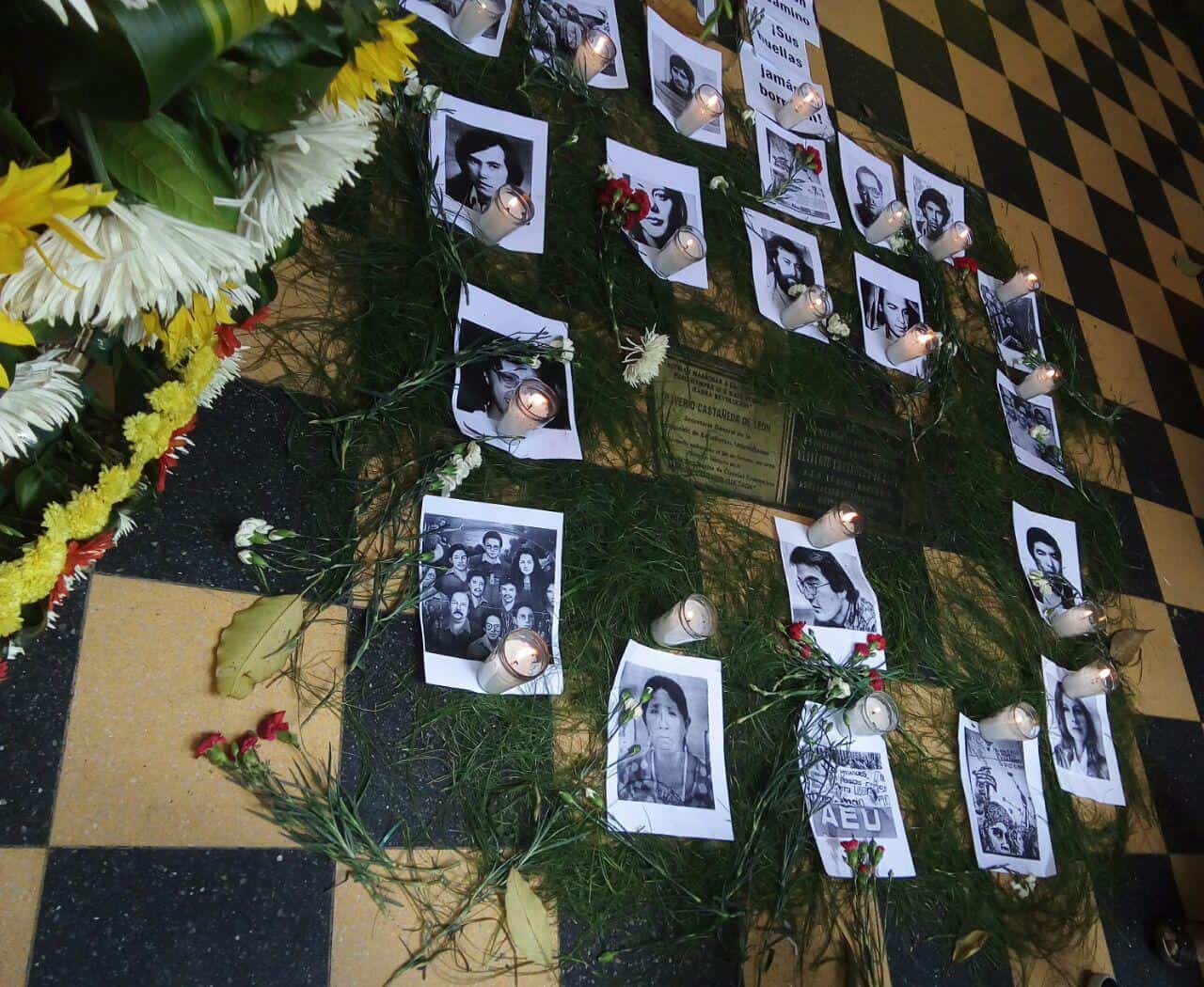 Pictures of disappeared people are placed with candles around a plaque marking the site where student organizer Oliverio Castañeda de León was assassinated.