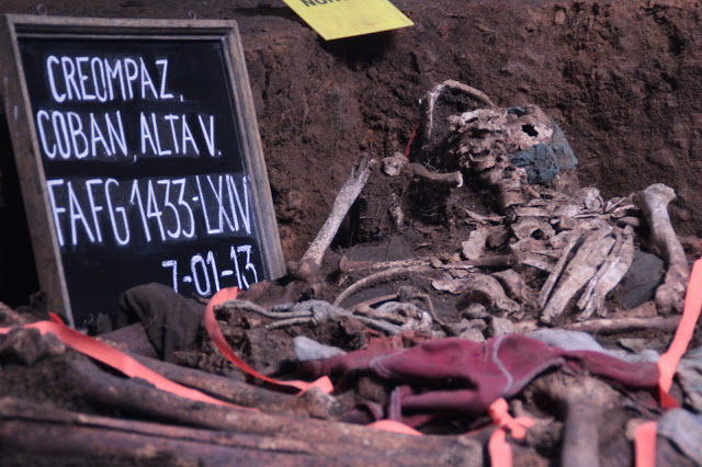 Left side shows a chalkboard reading "CREOMPAZ, Alta Verapaz" and the date, July 1, 2013. Next to the chalkboard are the uncovered human remains in an exhumed pit.