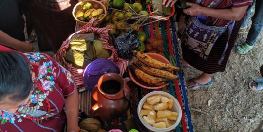 Women gather around a brightly colored table laden with fruits and drinks.