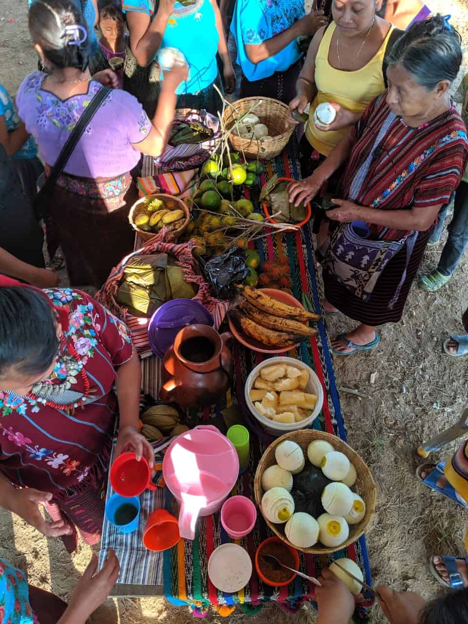 Women gather around a brightly colored table laden with fruits and drinks.