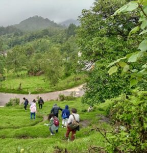  In the right foreground we can see some trees, then a road and several people walking downhill. In the background you can see another house and a very green landscape. // Se observa en primer plano del lado derecho unos árboles, después un camino y varias personas bajando. En el fondo se ven otra casa y un paisaje muy verde.