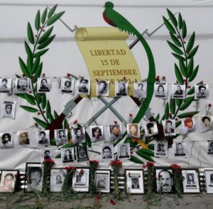Covering a giant poster with guatemalan national symbols, organizations put in the front pictures of the dissapeared and murder during the Internal Armed Conflict along with red carnations