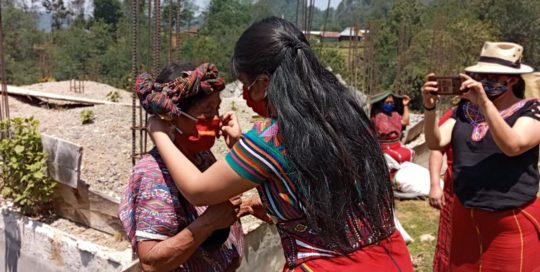 Una representante de la AJR le ayuda a pobladora a ponerse mascarilla. Foto: AJR