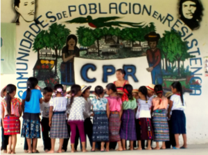 Picture of a group of children gathering together, in the wall there is a mural that reads CPR. Comunidades de Poblacion en Resistencia