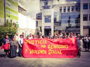 Communities Affected by Military Zone 21 Violence Call for Justice for Genocide and Sexual Violence. People hold a huge red banner that reads: "Justice for genocide and sexual violence / H.I.J.O.S."