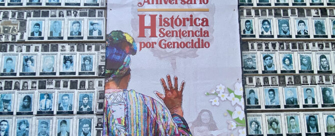 Behind a wallpaper of faces of the disappeared in the house of memory, hangs a banner on which in red letters reads the tenth anniversary of the historic sentence for genocide. Below is the back of an Ixil woman with her hand raised giving her testimony before Guatemalan courts.