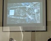 The photo above the court screen shows a photo of one of the graves where a skeleton can be seen. Below is the judge looking at the photo and on the left is the face of a man sitting in the row of lawyers. ////en foto se observa arriba la pantalla del tribunal se observa una foto de uno de las fosas donde se puede ver una osamenta. Abajo se observa al juez titular mirando la fotografia y se observa en la izquierda el rostro de un hombre sentado en la fila de abogados