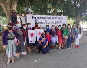 A group of women wearing facemask and some of them purple scarfs pose in Guatemala Central Park during the International Women´s day conmemoration, some of them hold a sign that reads: For a life free of violence against women"