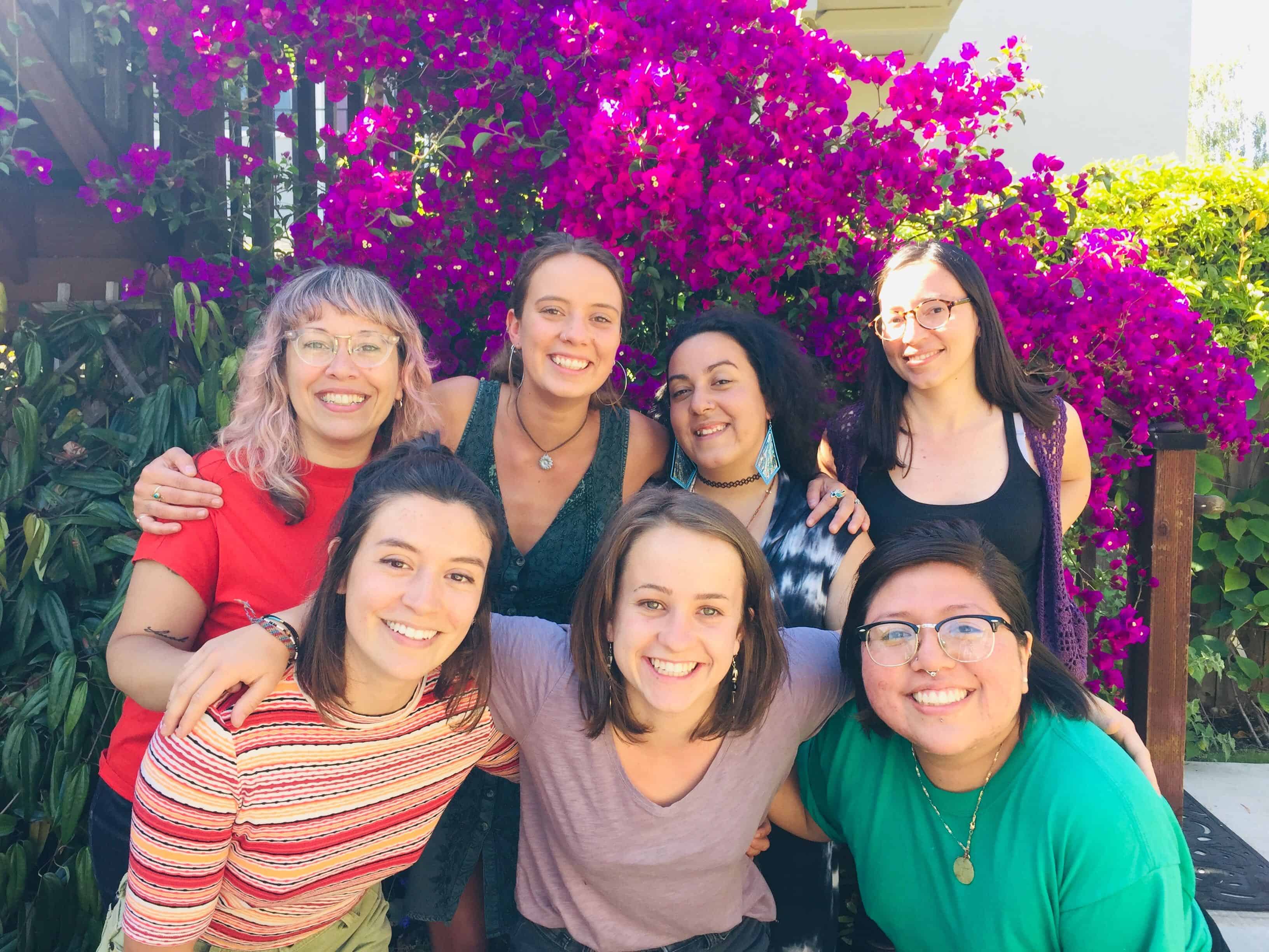 A photograph of 7 smiling people of color in front of a blooming tree.