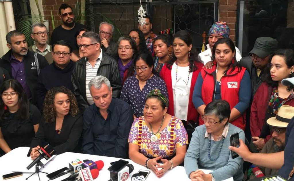 A large group of people gather around a table with microphones. In the foreground are Rigoberta Menchú and other famous Guatemalan leaders of social movements.