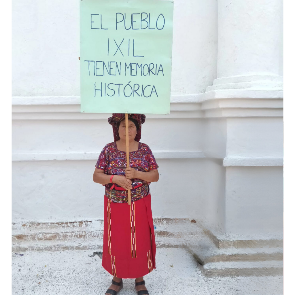 A woman with traditional dress, holds a banner with a spanish quote: The Ixil People have historical memory.