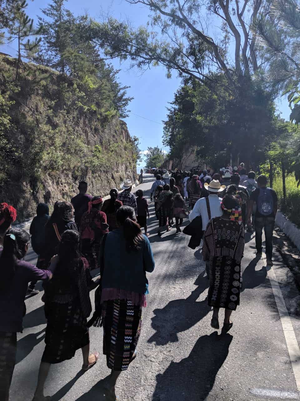 Photograph of Mayan people walking up a hill surrounded by trees.