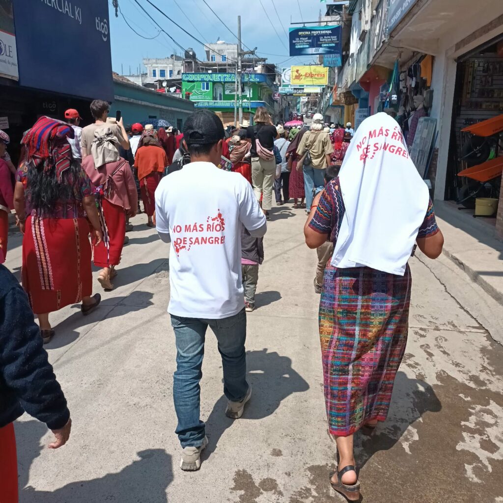 the image above shows political party advertisements in chajul for the elections, while a group marches through the streets. Close up you can see participants on the left wearing red clothing, typical of the Ixil region, while two people wear a white t-shirt with red letters that say No more rivers of blood.