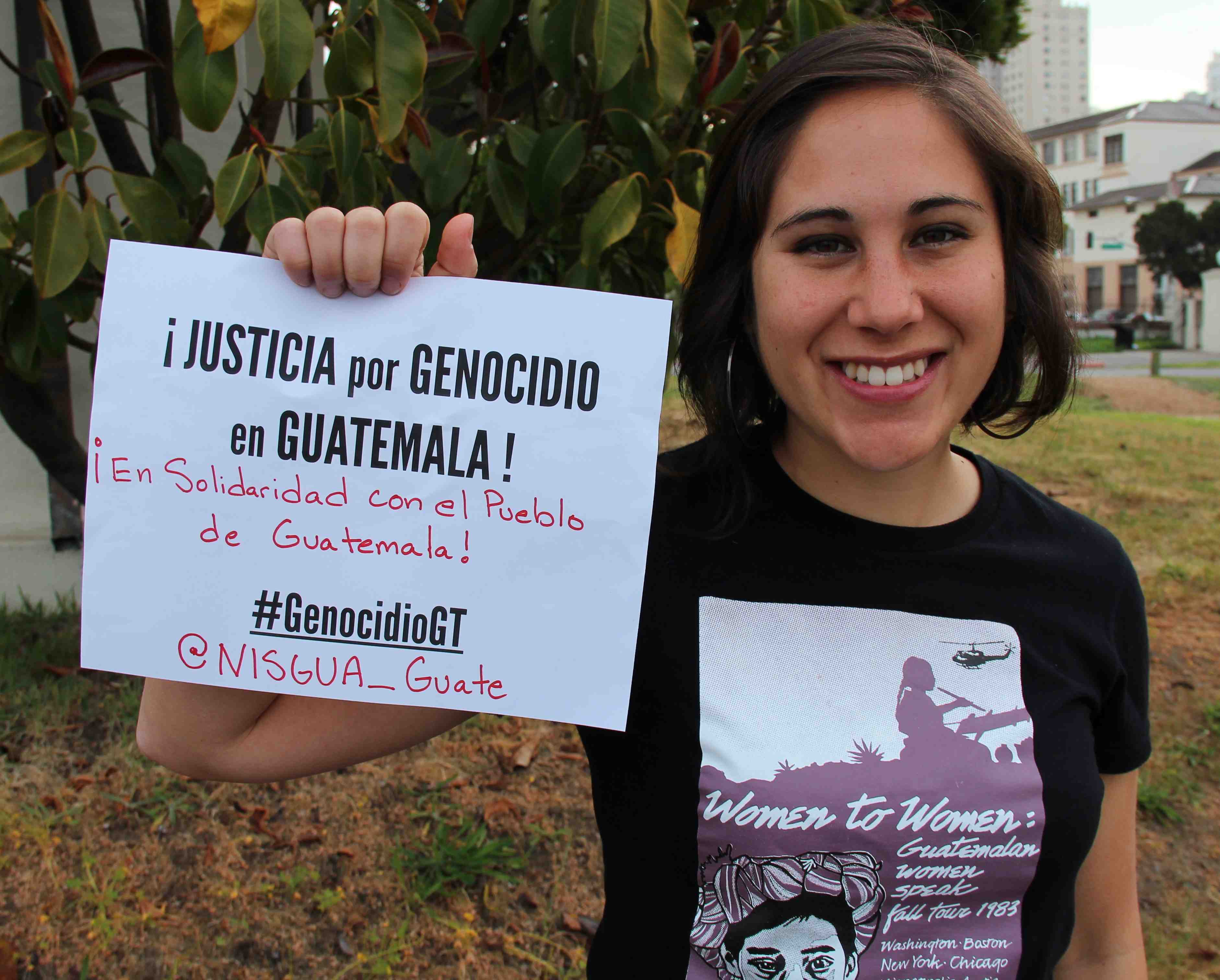 A photograph of a NISGUA organizer holding a sign that reads "Justicia por genocidio en Guatemala!"