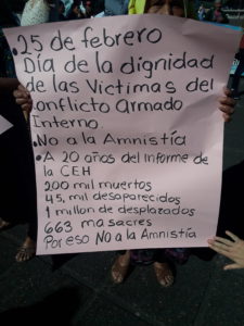 A survivor of the genocide holds a sign that says "February 25 / Day of Dignification for the Victims of the Internal Armed Conflict / No to the amnesty / 20 years after the report by the CEH / 200,000 dead / 45,000 disappeared / 1 million displaced people / 663 massacres / Because of this, no to the amnesty."