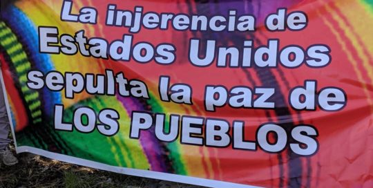 A sign reads, "The interference by the United States buries the people's peace."