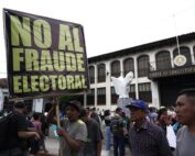 [ENG] A photograph of people in a protest outside a building with many windows, the building signs read "Constitutional Court" and a person socialized as a man, holding a sign that reads: "No to electoral fraud". [ESP] Una fotografía de personas en un plantón afuera de un edificio con muchas ventanas, en el edificio se lee “Corte Constitucional” y una persona socializada como hombre, sostiene un cartel que dice: “No al fraude electoral”