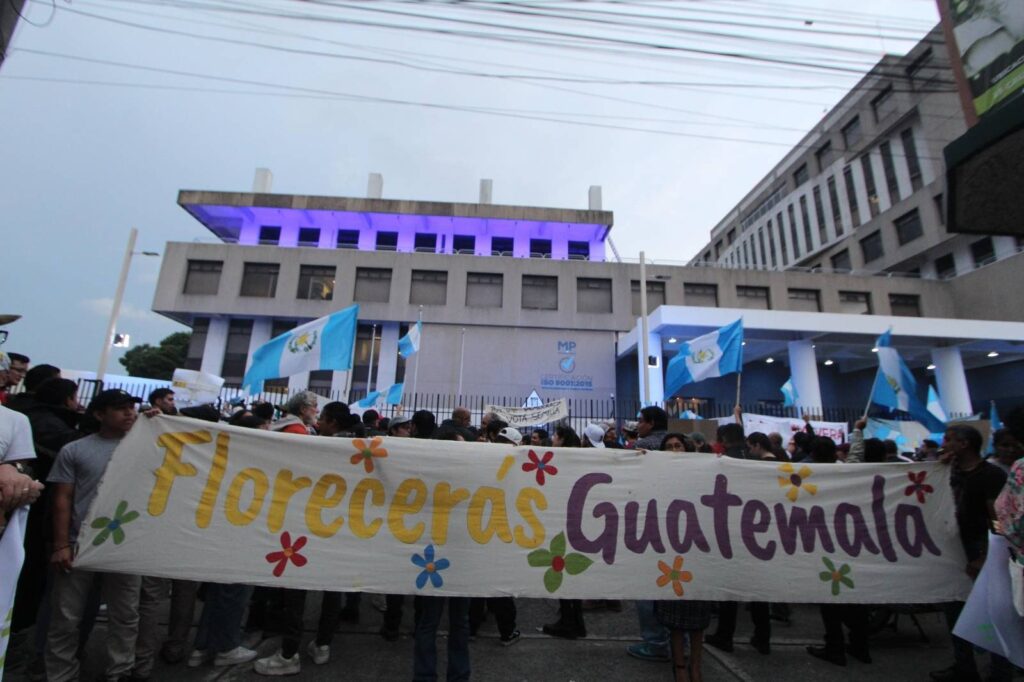 En la plaza de Derechos Humanos de Guatemala, personas se manifiestan y cargan una pancarta que dice: “Florecerás Guatemala” con flores pintadas de muchos colores.