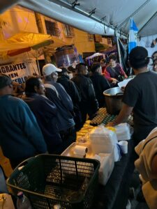 [ESP] Bajo una tienda blanca, una fila de personas espera a que le sirvan comida [ENG] Under a white tent, a line of people wait for food to be served.