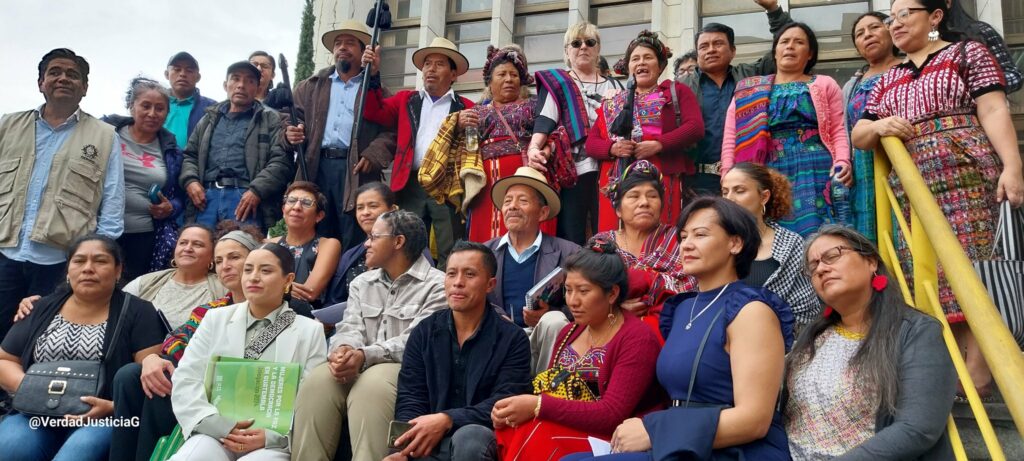 Sentados y parados afuera de la torre de tribunales se observa a un grupo de hombres y mujeres sobrevivientes del genocidio en la region Ixil, acompañados de las autoridades ancestrales ixiles con su baston de mando, miembros de organizaciones sociales entre otros.