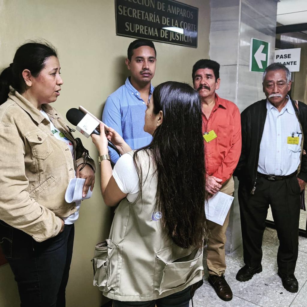 A journalist holds a microphone to a woman who is speaking while three men listen.
